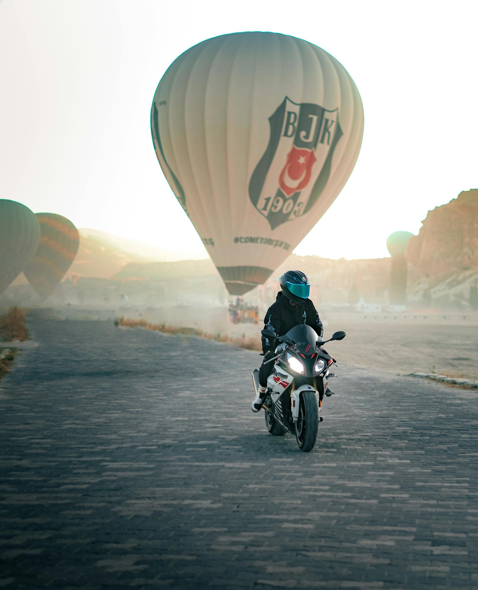 Dynamic scene of a motorcyclist riding near hot air balloons in Cappadocia, Turkey.